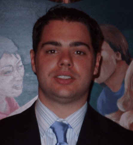 A man in suit and tie standing next to a painting.