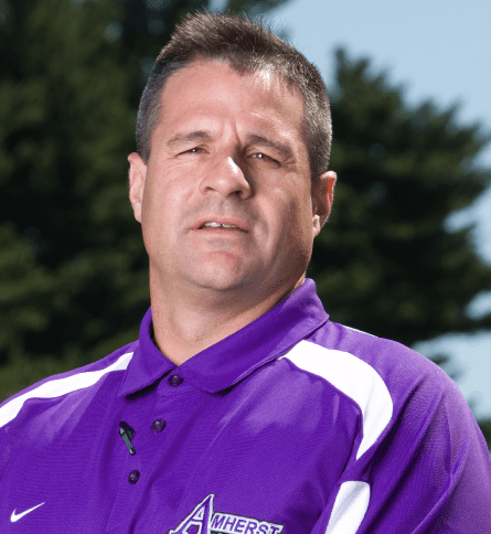 A man in purple shirt standing next to tree.