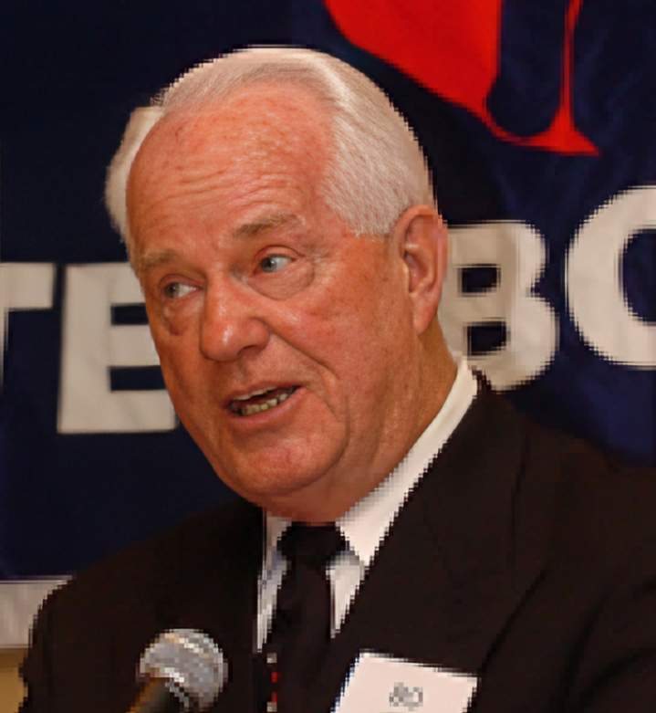 A man in suit and tie speaking at a microphone.