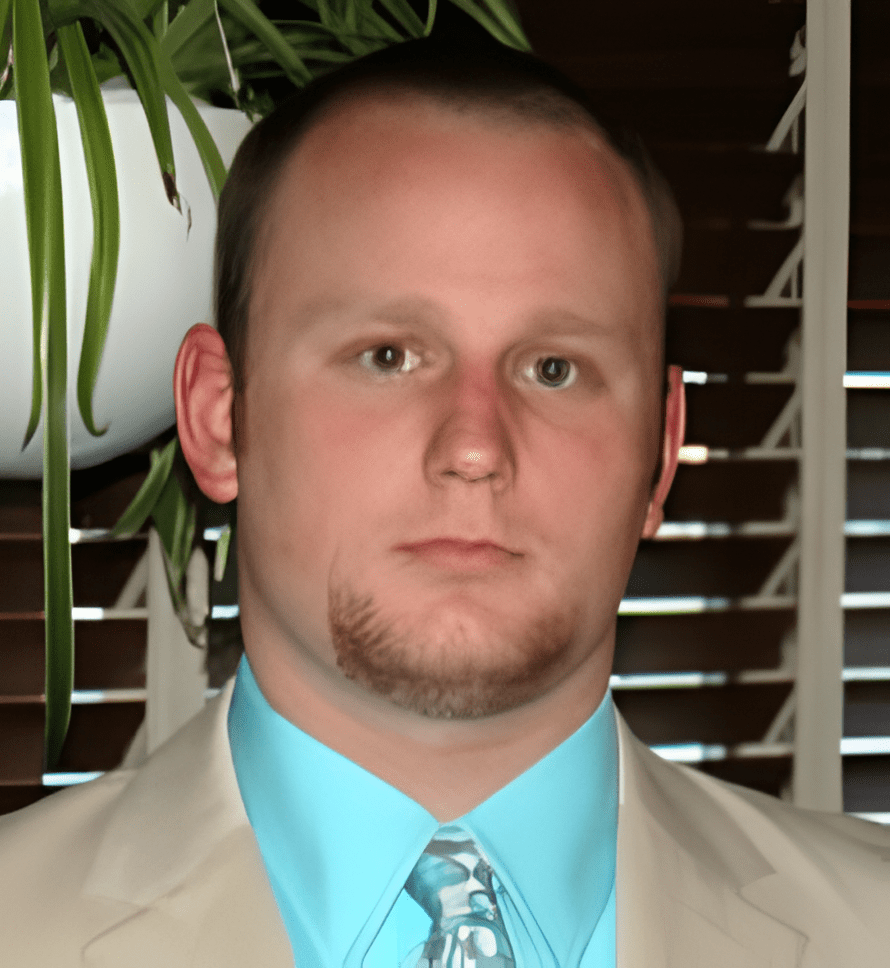 A man in a suit and tie standing next to a plant.