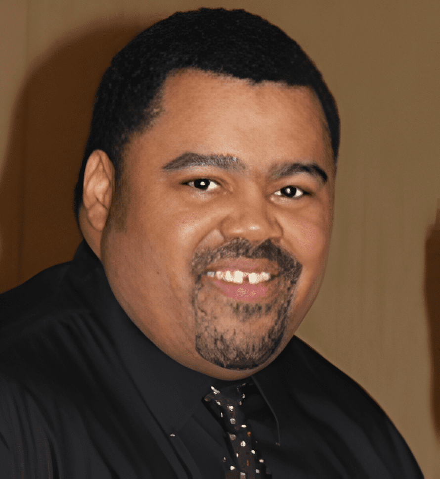 A man in black shirt and tie smiling for the camera.