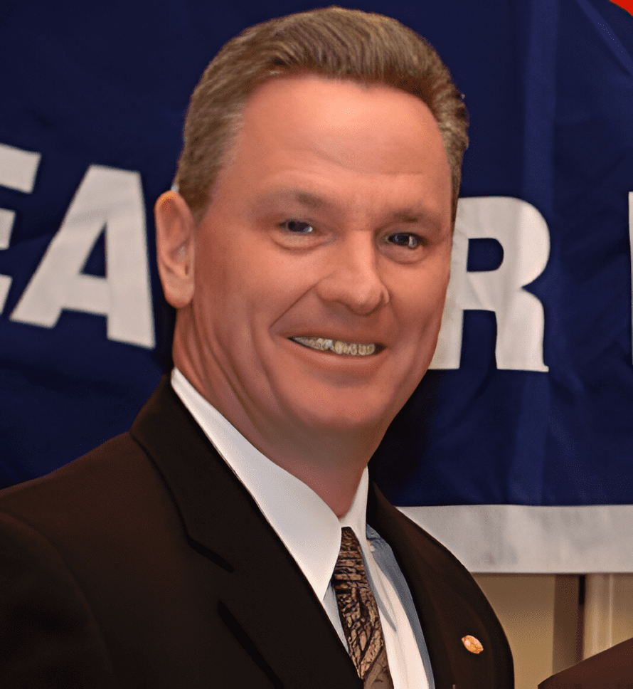 A man in suit and tie standing next to a blue banner.