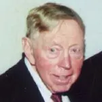 A man in suit and tie with white hair.